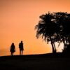 silhouette of man and woman standing on sand during sunset