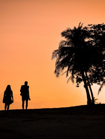 silhouette of man and woman standing on sand during sunset