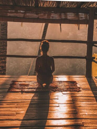 woman meditating on floor with overlooking view of trees