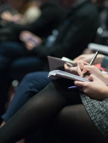 selective focus photography of people sitting on chairs while writing on notebooks