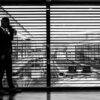 silhouette of man standing beside clear glass wall while using smartphone