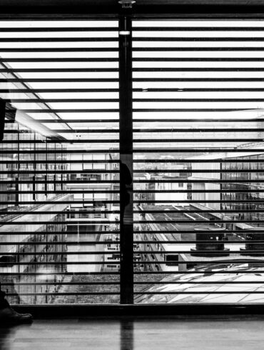 silhouette of man standing beside clear glass wall while using smartphone