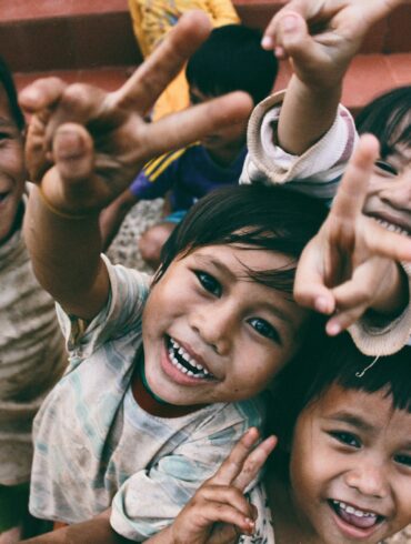 five children smiling while doing peace hand sign