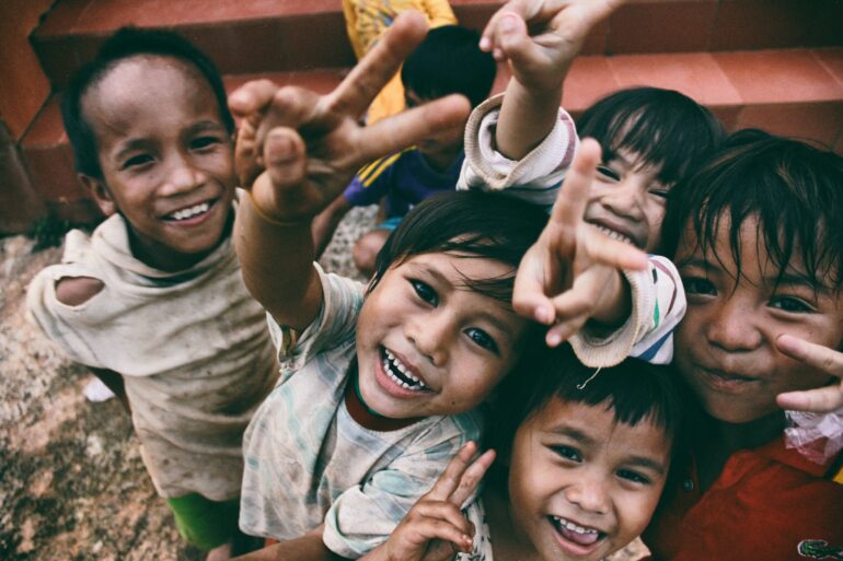 five children smiling while doing peace hand sign