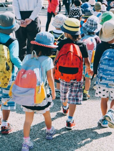 group of people wearing white and orange backpacks walking on gray concrete pavement during daytime