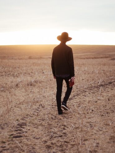 man walking on dried plain while looking towards the sun on horizon