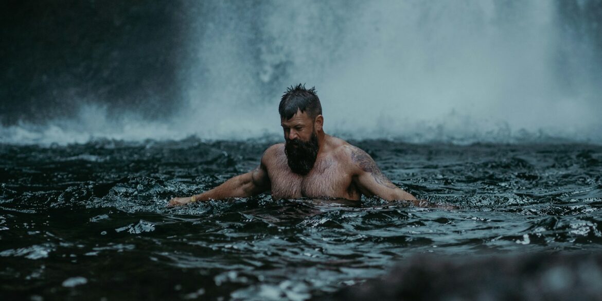 a man swimming in the water in front of a waterfall
