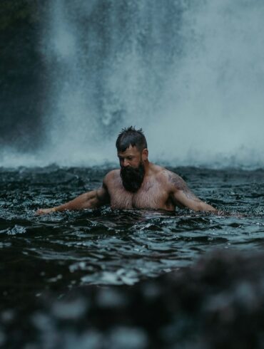 a man swimming in the water in front of a waterfall
