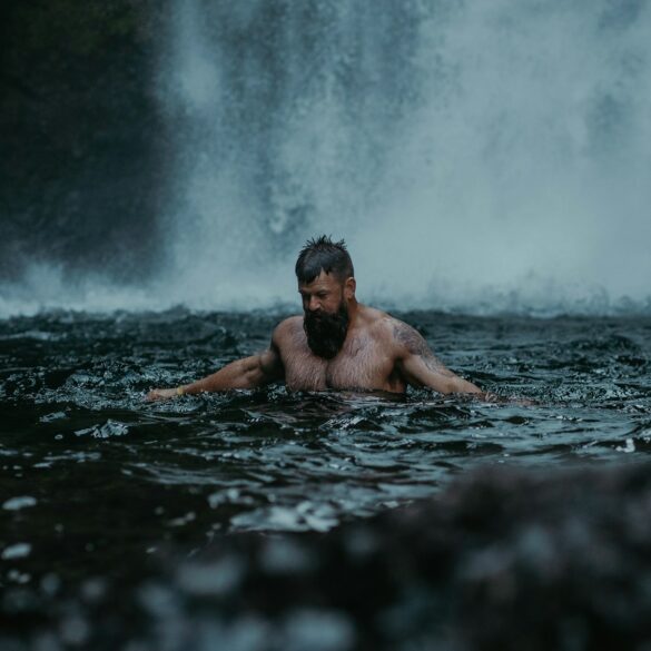 a man swimming in the water in front of a waterfall