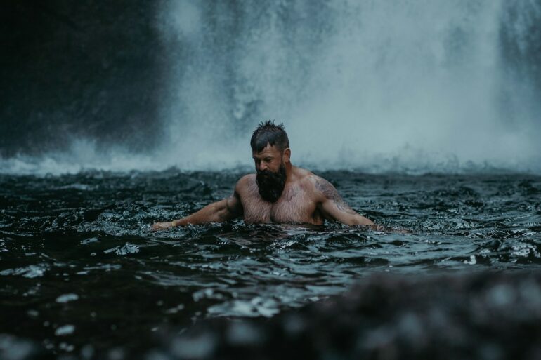 a man swimming in the water in front of a waterfall