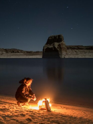 person sitting beside bonfire on seashore