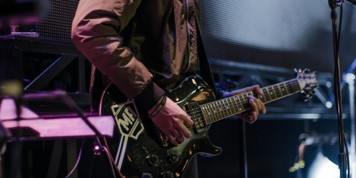 man playing black electric guitar beside black microphone with stand