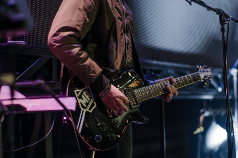 man playing black electric guitar beside black microphone with stand