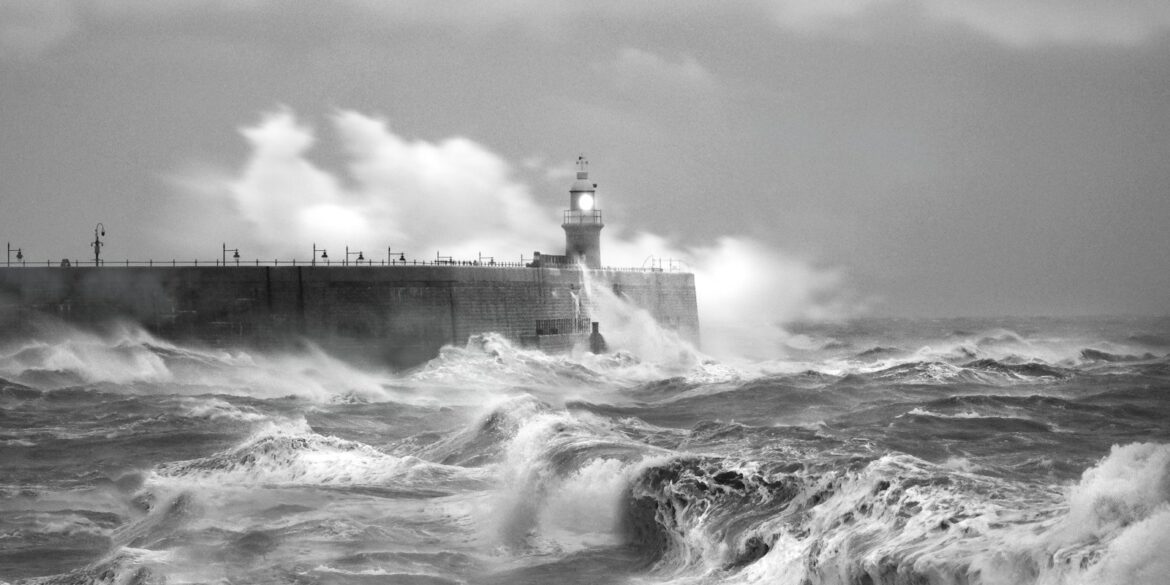 grayscale photo of sea waves crashing on concrete wall