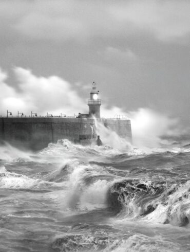 grayscale photo of sea waves crashing on concrete wall