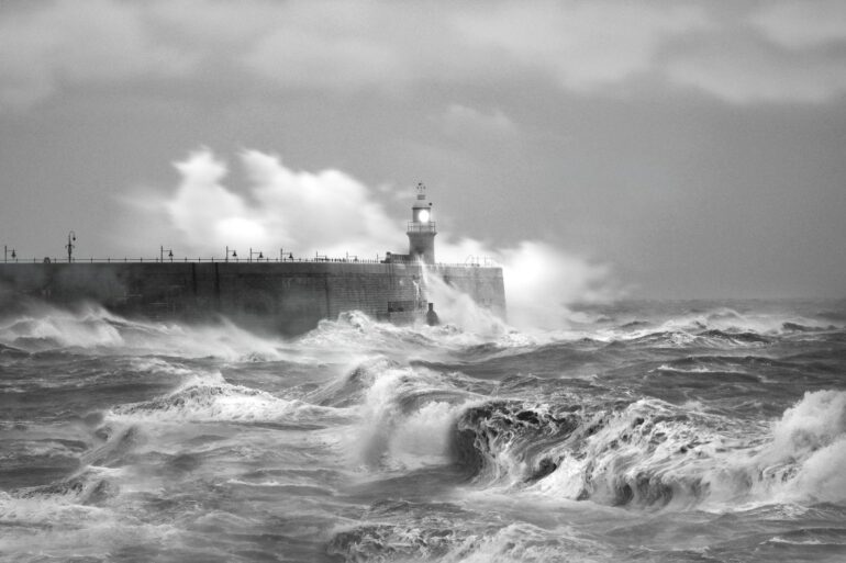 grayscale photo of sea waves crashing on concrete wall