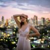 woman in white spaghetti strap dress wearing brown sun hat standing on the street during daytime