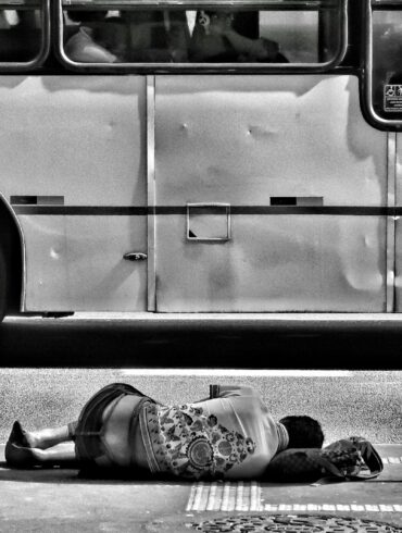 grayscale photography of person laying on ground near bus