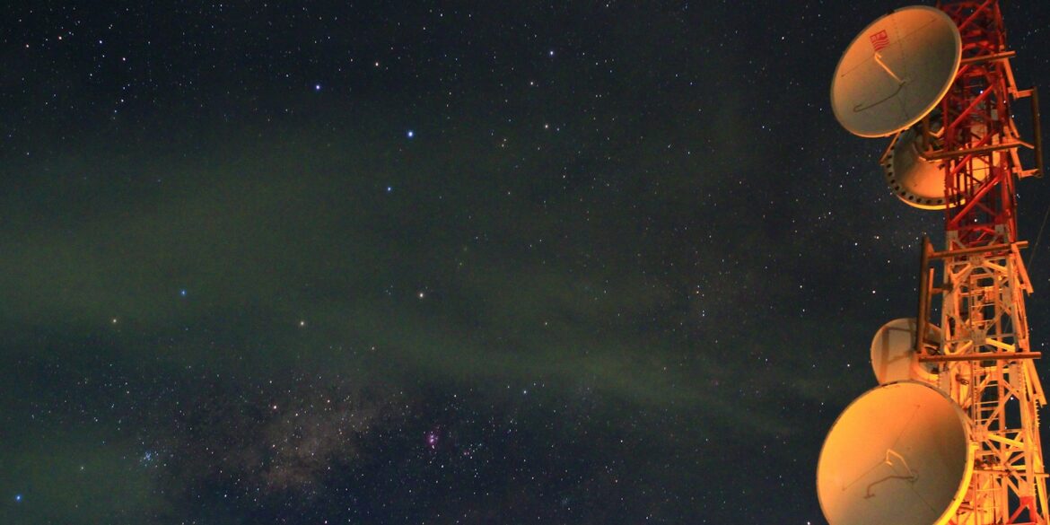 astrophotography red and white tower with satellites under milky way