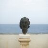 a statue of a head on a pedestal by the water