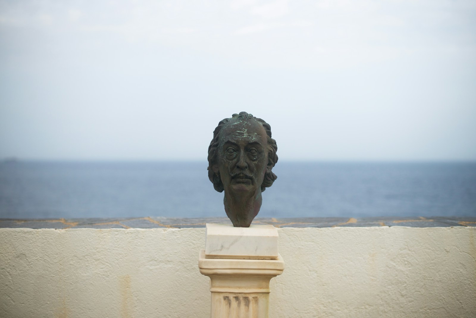 a statue of a head on a pedestal by the water
