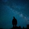 a man standing on top of a hill under a night sky filled with stars