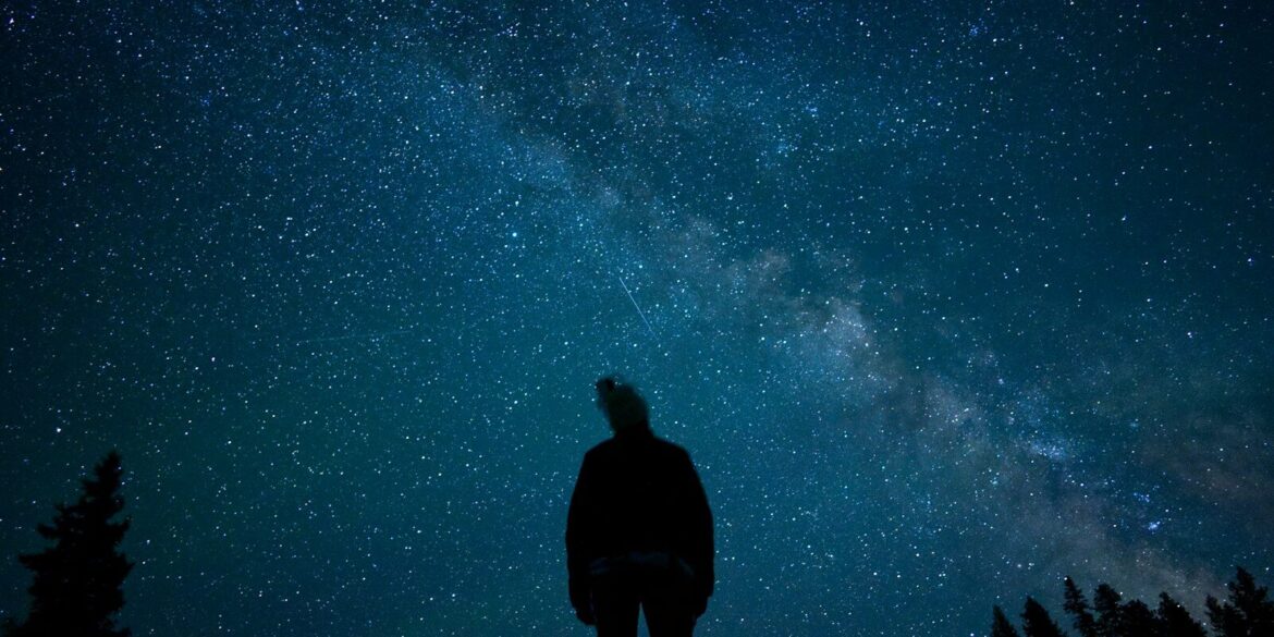a man standing on top of a hill under a night sky filled with stars