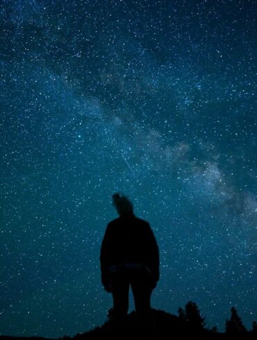 a man standing on top of a hill under a night sky filled with stars