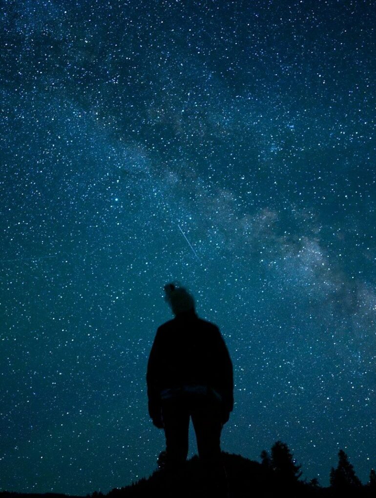 a man standing on top of a hill under a night sky filled with stars
