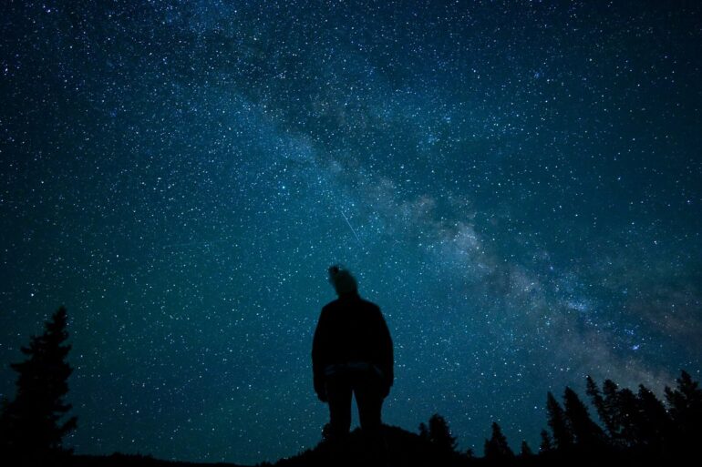 a man standing on top of a hill under a night sky filled with stars