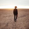 man walking on dried plain while looking towards the sun on horizon