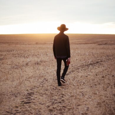 man walking on dried plain while looking towards the sun on horizon