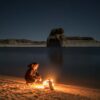 person sitting beside bonfire on seashore